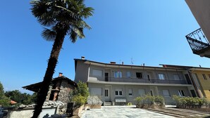 A multi-story building with balconies, a stone structure to the left, and a palm tree in the foreground.