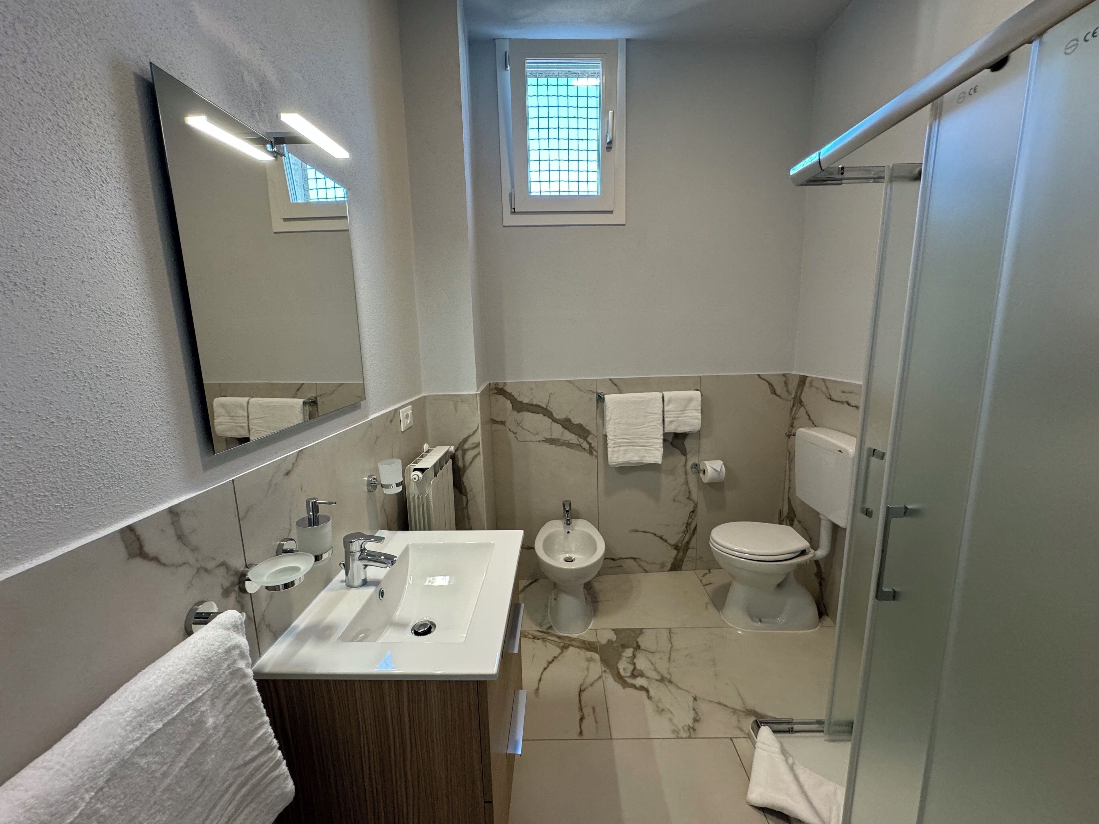 Une salle de bain moderne avec un sol carrelé en marbre, un lavabo avec un miroir au-dessus, des toilettes et un espace douche.