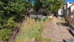 Eine Wohngegend an einem Hang mit einer Holztreppe, die zu einem Haus führt, umgeben von üppiger Vegetation und einem Schotterweg.