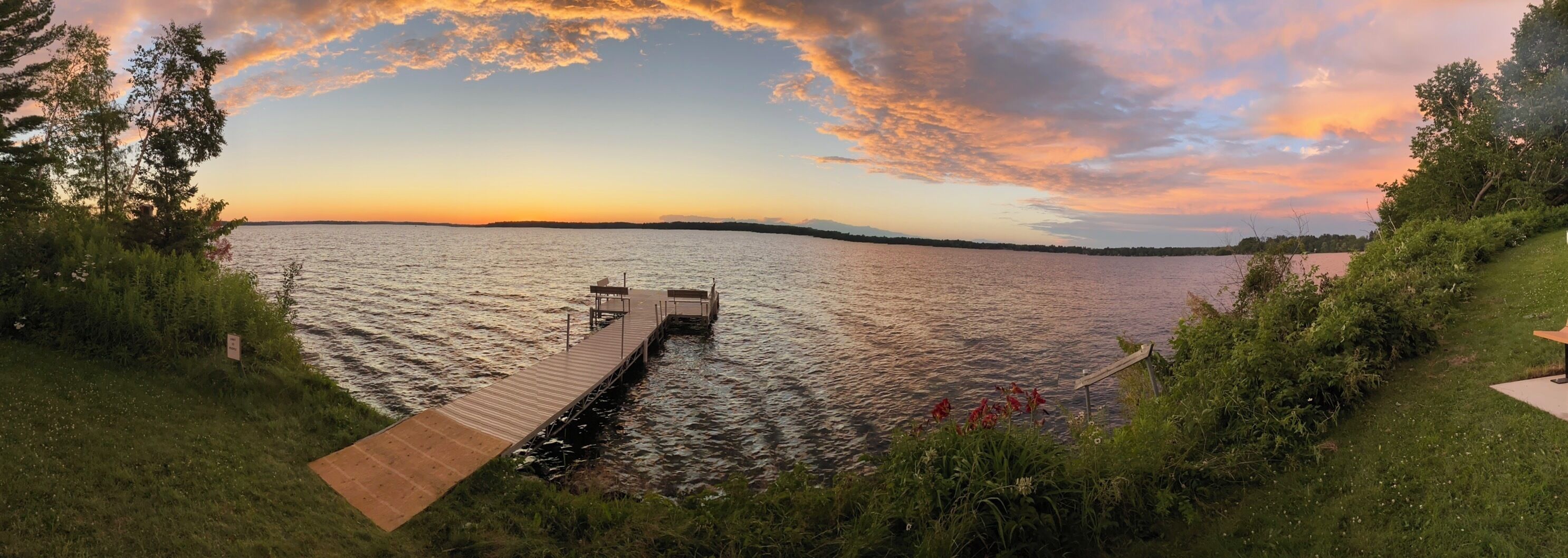 A wooden dock extending into a calm lake with a sunset in the background.