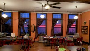 Un comedor con varias mesas y sillas, ventanas amplias con cortinas y ventiladores de techo.