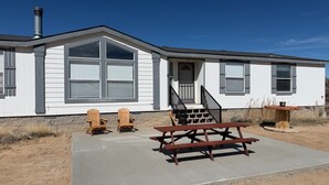 Une maison de plain-pied avec un porche à l’avant, deux fauteuils Adirondack, un banc en bois et une cheminée.