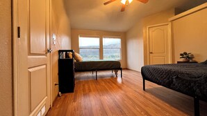 Une chambre avec un ventilateur de plafond, deux lits, une fenêtre donnant sur un beau paysage et une porte.
