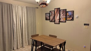 Un coin repas avec une table et des chaises, un lustre, un ensemble de tableaux encadrés accrochés au mur et un panneau indiquant qu'il est interdit de fumer.