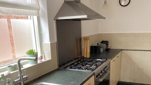 A kitchen with a stainless steel sink, wooden cabinets, a gas stove, and a black tiled floor. - Right in the center across from the stores  (Udenhout)