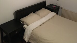 A bedroom with a bed, a nightstand, a bedside table, a wall-mounted air conditioner, and a wall socket. - Right in the center across from the stores  (Udenhout)