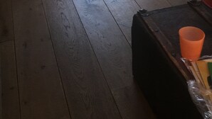A room with wooden flooring, a white sofa, a small round table, and a black ottoman with an orange cup. - Right in the center across from the stores  (Udenhout)