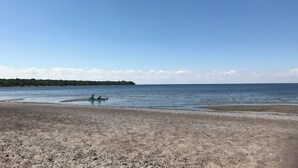 Une plage avec un ciel dégagé, une eau calme et une étendue de terre boisée qui se profile à l’horizon.