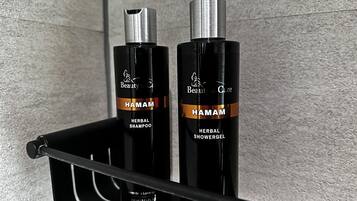 Dos botellas de Champú y Gel de Ducha Herbal Hamam sobre un estante negro frente a una pared con textura.