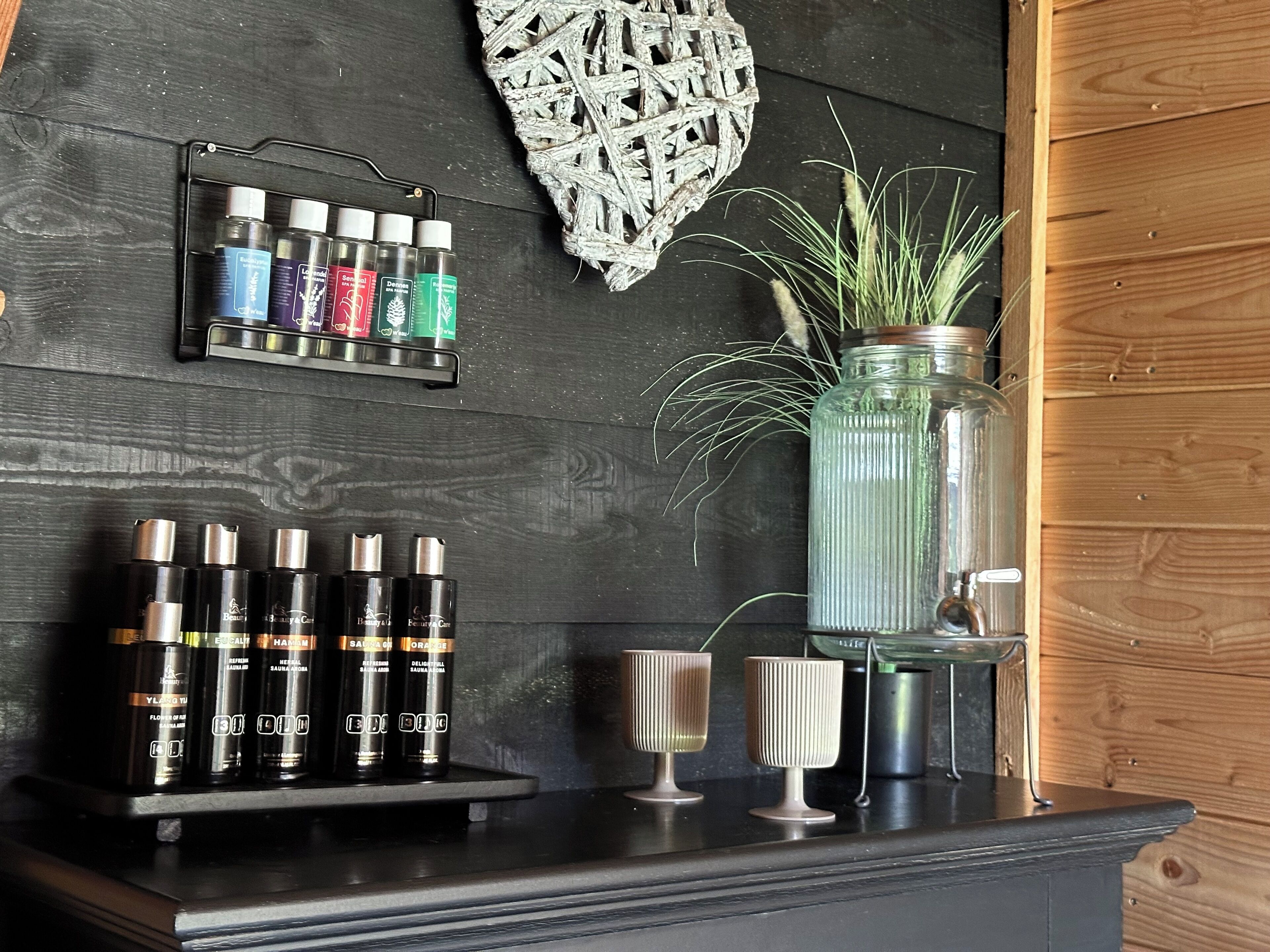 Een plank met verschillende haarverzorgingsproducten, een decoratieve wandhanger en een glazen pot met een plant.