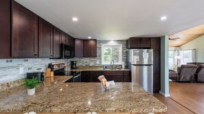 A modern kitchen with dark wood cabinets, a granite countertop, stainless steel appliances, and a view of the outdoors. - The Lake Life by Avantstay Lakefront + View + Hot Tub (Pocono Lake)