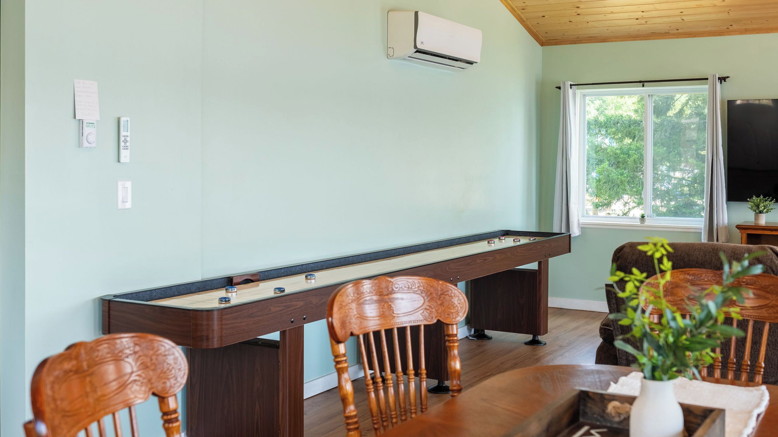 A pool table with chairs, a television, and a window with a view of trees.