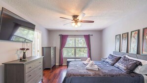 A bedroom with two beds, a ceiling fan, a dresser, a window with curtains, and framed artwork on the wall.