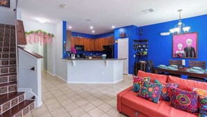 A modern kitchen with wooden cabinets, a central island, and a dining area with a red sofa and colorful pillows.