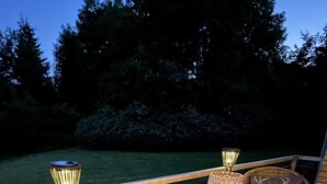 An outdoor patio with wicker furniture, including a round table and two chairs, and two table lamps.