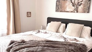 A bedroom with a bed, a headboard, a wall-mounted artwork of a deer, and a window with curtains.