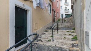 En smal gade med brostensbelagte trin, der fører op til en bygning med en sort dør og en hvid facade.