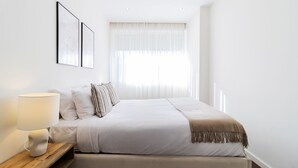 A neatly arranged bedroom with a large bed, a bedside table with a lamp, and a window with sheer curtains. - 2BR Wonder in the City Center by LovelyStay (Porto)