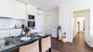 A modern kitchen with white cabinets, a glass dining table set with plates and glasses, and a potted plant. - 2BR Wonder in the City Center by LovelyStay (Porto)