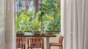 A balcony with a table set for dining, surrounded by chairs, overlooking a tropical garden.