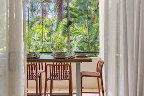 A balcony with a table set for dining, surrounded by chairs, overlooking a tropical garden.