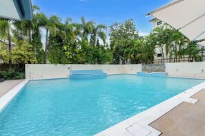 A swimming pool with a clear blue water, surrounded by a white wall and palm trees.