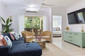 A living room with a sofa, two armchairs, a coffee table, a TV, and a dining area with chairs.