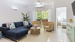 A living room with a sofa, coffee table, wicker chairs, and a TV.