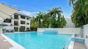 A swimming pool with lounge chairs, a water feature, and a multi-story building with balconies.