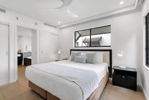 A modern bedroom with a large bed, bedside tables, a mirror, and a view of the outside.
