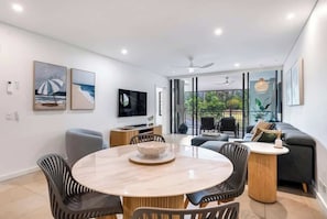 A modern living room with a round dining table, comfortable seating, a flat-screen TV, and artwork on the walls.