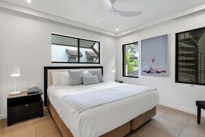 A modern bedroom with a bed, bedside table, nightstand, ceiling fan, and large windows.