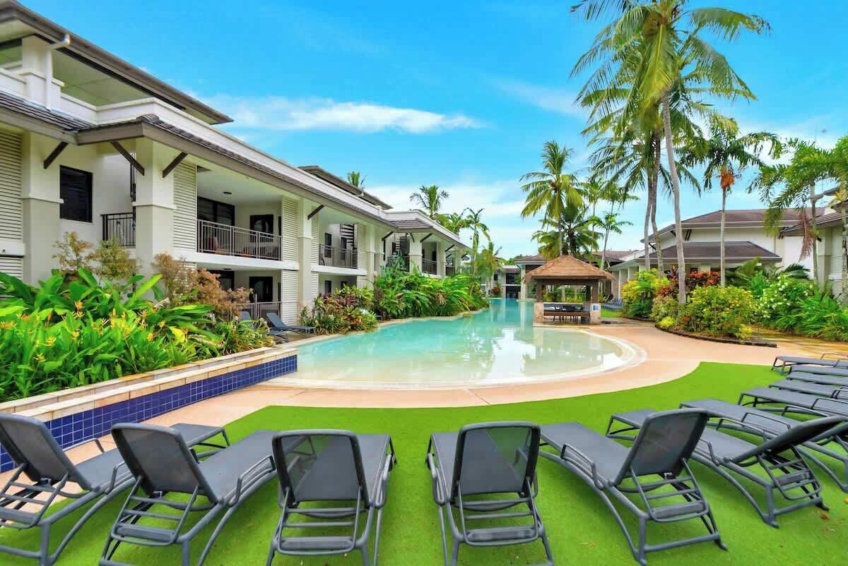 Un espace piscine comprenant des chaises longues, une piscine et un bâtiment doté de balcons.
