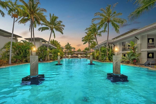A swimming pool with palm trees and hotel buildings in the background.