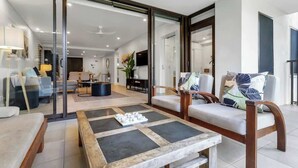 Ein modernes Wohnzimmer mit Glastür zu einem Essbereich, einem Holztisch und einer Couch mit gemusterten Kissen.