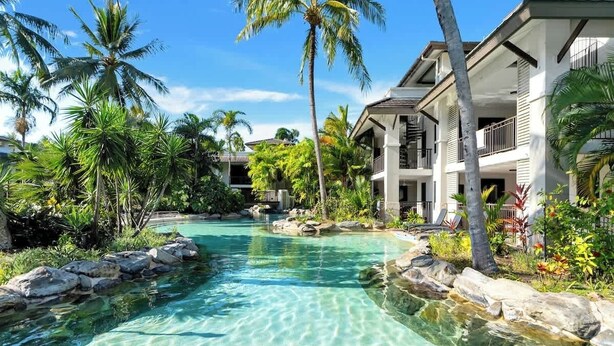 Ein Resort mit einem klaren Pool, Palmen und einem zweistöckigen Gebäude mit Balkonen.