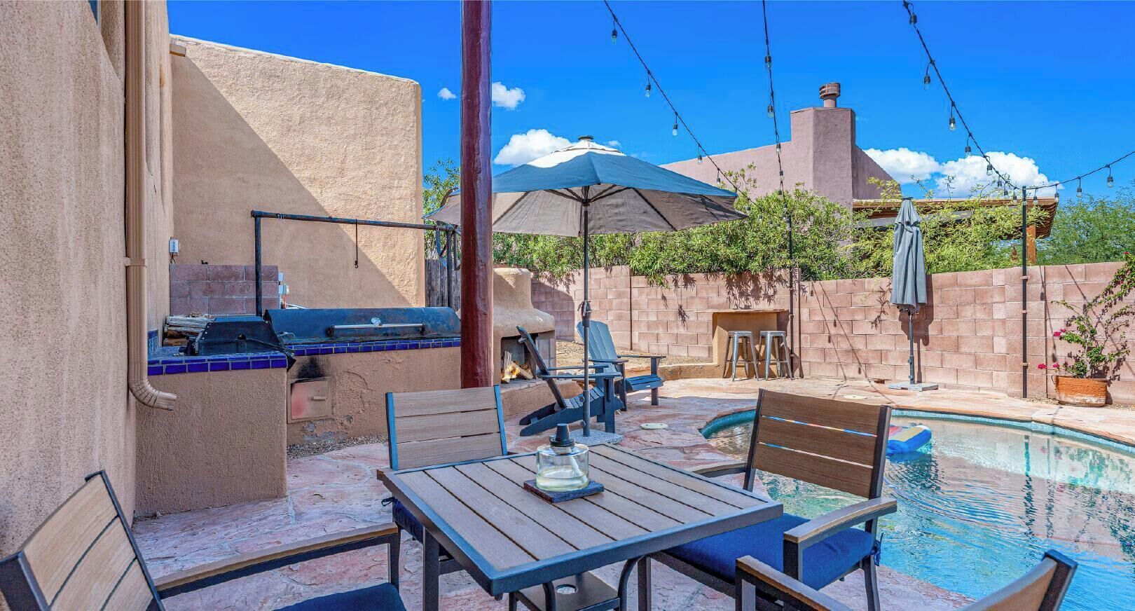Un espace aménagé au bord de la piscine, avec un barbecue, des sièges d’extérieur et une vue sur un bâtiment en arrière-plan.