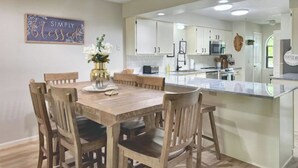 Une cuisine moderne avec des meubles blancs, un îlot central et un coin repas comprenant des chaises et une table en bois.