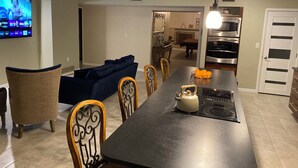 Et moderne køkken med en stor ø, mikroovn, ovn og elkedel. Der er spiseplads med sofa og stole.