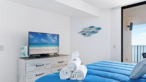 A bedroom with a bed, a TV on a dresser, and a view of the sea.