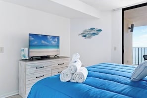 Une chambre avec un lit, un téléviseur posé sur une commode et une vue sur la mer.