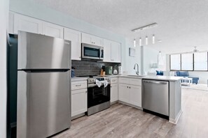 A modern kitchen with stainless steel appliances, white cabinetry, and a grey tiled backsplash.
