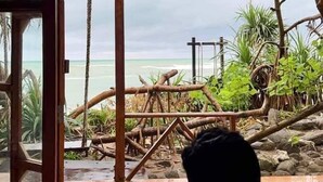 A room with a large window overlooking a beach with wooden structures and plants. - Shurjo Snan Twin Beach Resort (Saint Martin's Island)