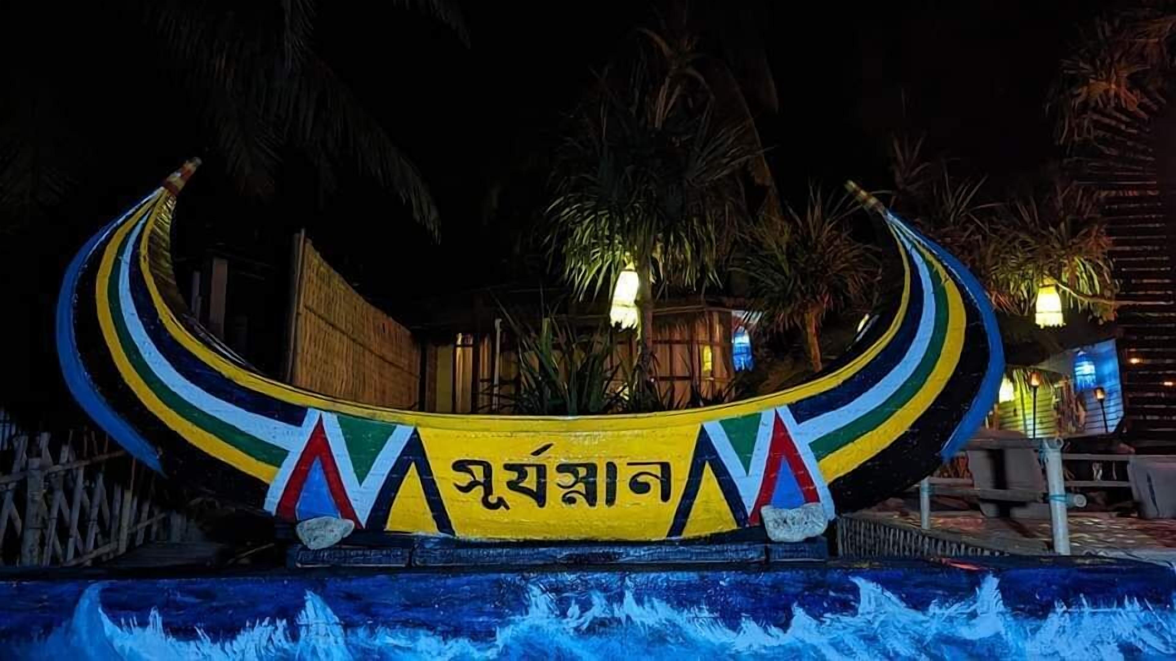 A boat-shaped structure with colorful stripes and text, surrounded by water and palm trees.