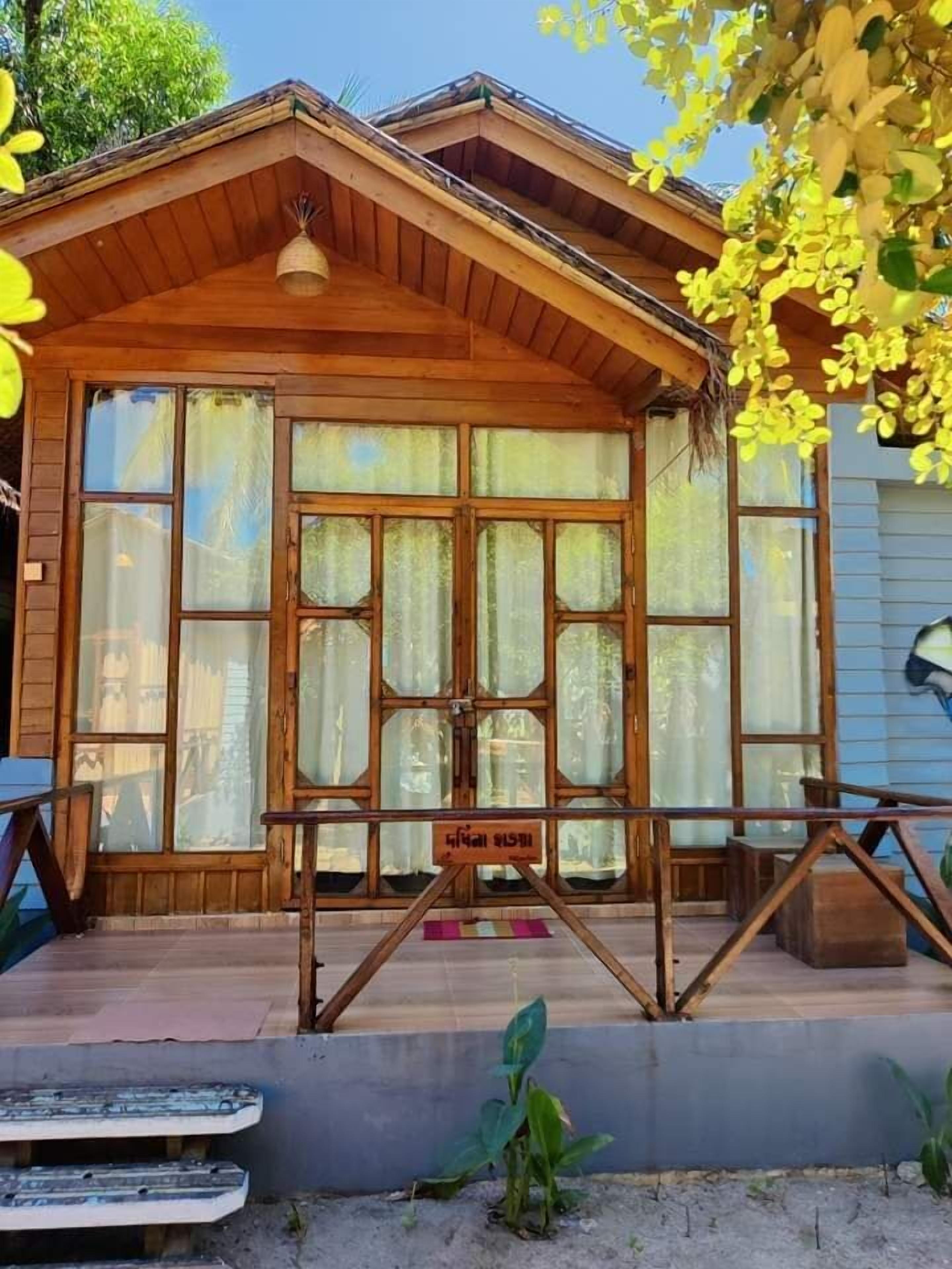 A wooden cabin with large windows, a porch, and a sign in a foreign language.