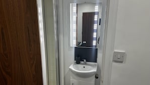 A bathroom with a glass shower enclosure, a white sink, and a mirror with lights. - London Road Studio Retreat in Leicester (Leicester)