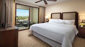 Una camera d'albergo con un letto grande, una scrivania con un computer, una sedia, un balcone con tavolo e sedie e una ventola a soffitto.