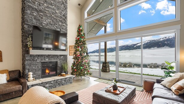 Ein geräumiges Wohnzimmer mit Kamin aus Stein, einem großen Fenster mit Bergblick und einem geschmückten Weihnachtsbaum.