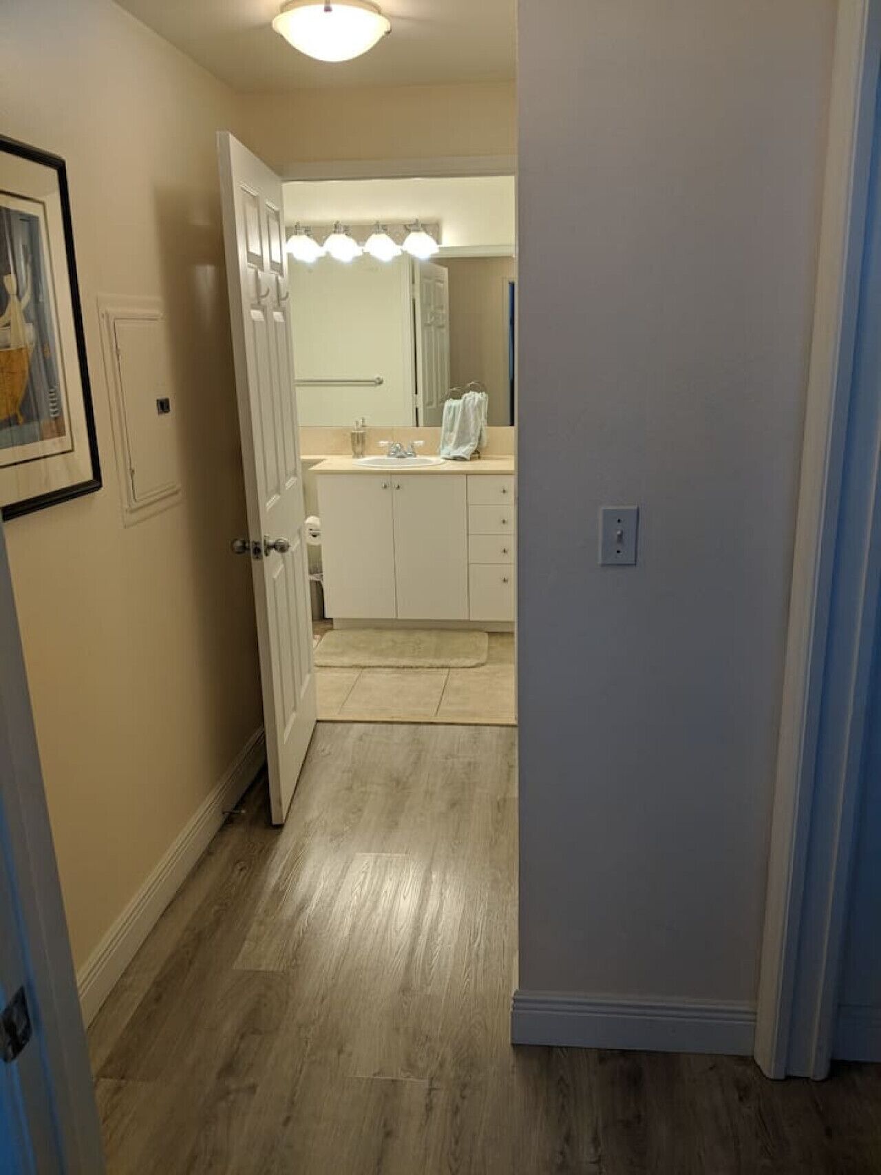 Un couloir menant à une salle de bain équipée d’un lavabo, d’un miroir et d’un porte-serviettes.