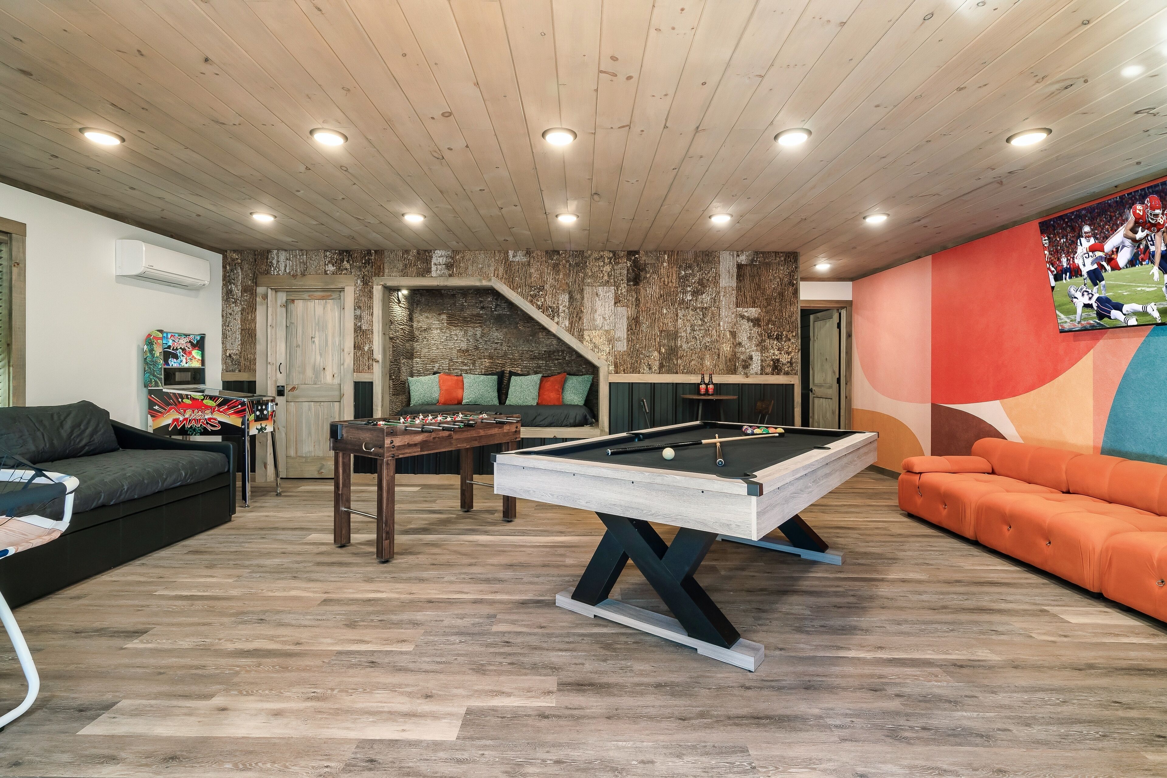 A cozy living room with a pool table, a sofa, and a colorful mural.